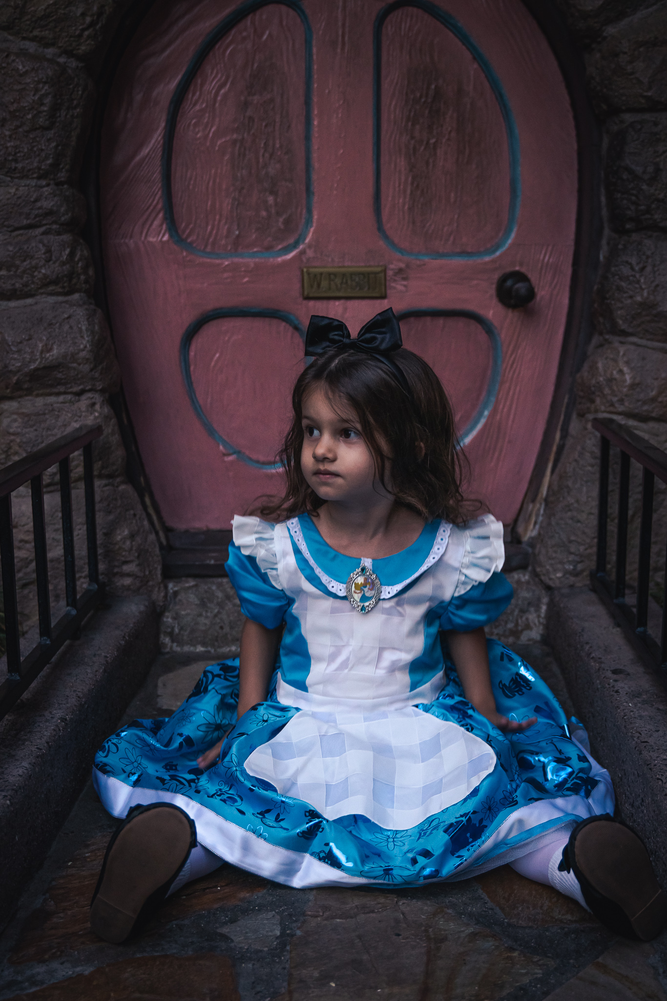 A small girl dressed at Alice in Wonderland sits outside of the White Rabbits Home in Fantasyland at Disneyland in Anaheim, California